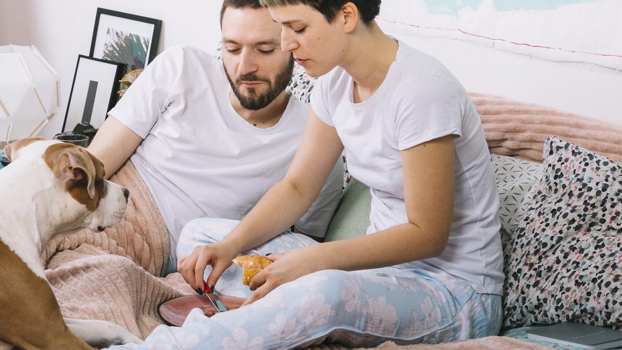 Couple feeding their dog by hand on a bed, highlighting manual workarounds when automatic food subscriptions fail
