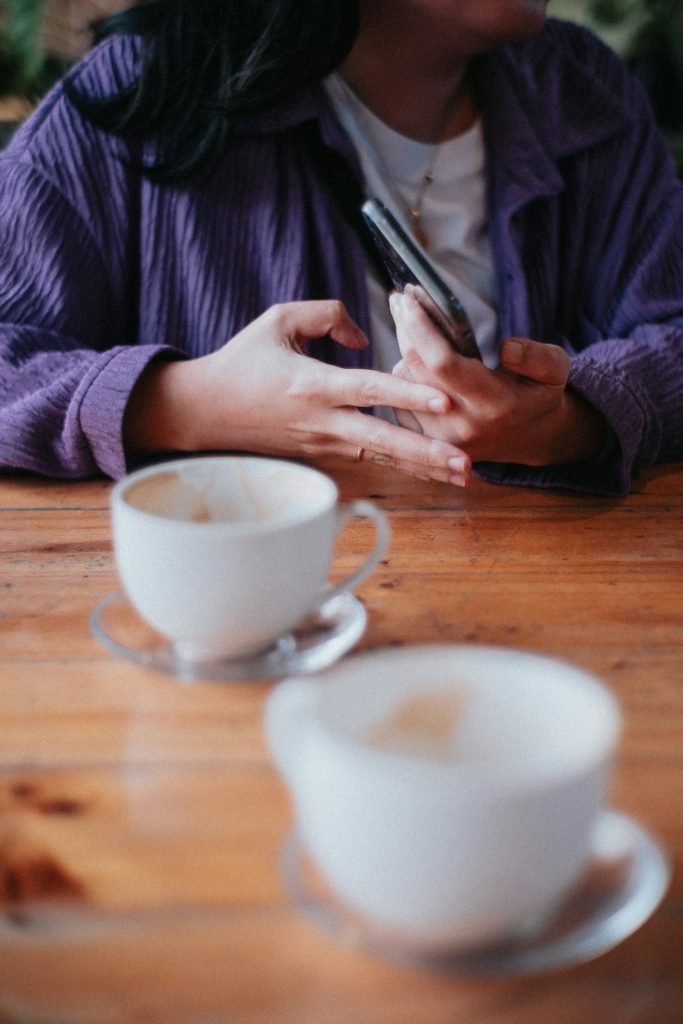 Person holding a phone at a cafe table with coffee cups