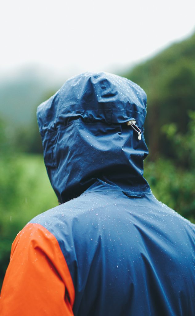 Hiker in a blue and orange waterproof jacket looking at green hills