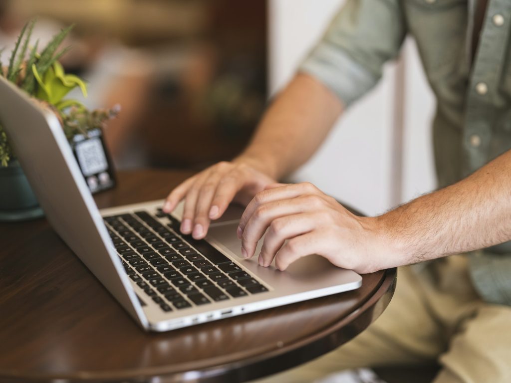 Hands typing on a laptop at a wooden cafe table