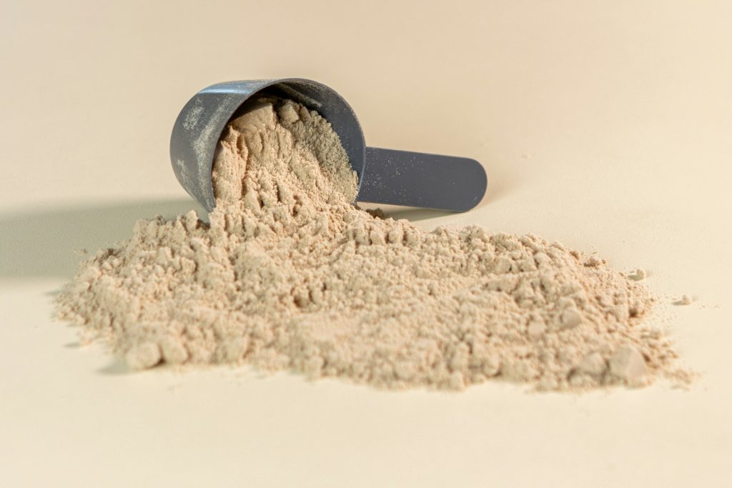 Scoop of protein powder spilling onto a warm neutral surface